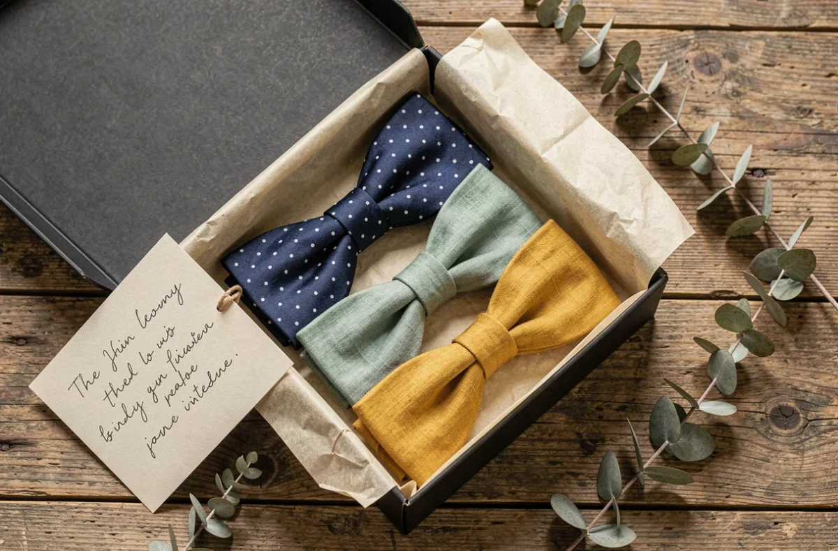Boîte cadeau ouverte contenant des nœuds papillons originaux en différentes matières, idée cadeau élégant pour homme