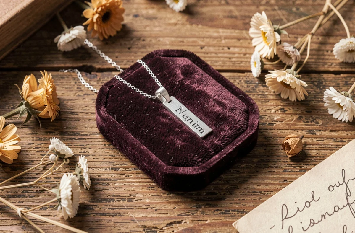 Collier pendentif en argent gravé pour enfant posé sur plateau de bijoux avec fleurs séchées et note manuscrite