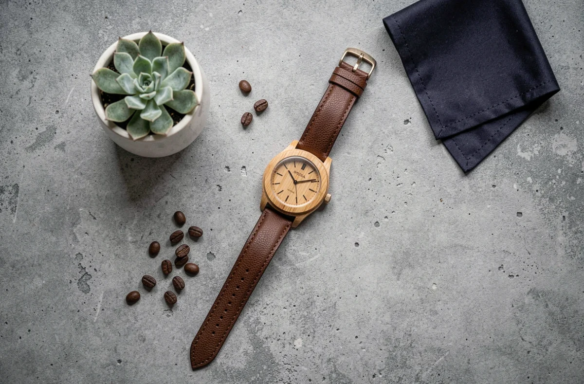 Montre bois et cuir posée en flat lay sur béton gris avec accessoires lifestyle, vue de dessus style éditorial